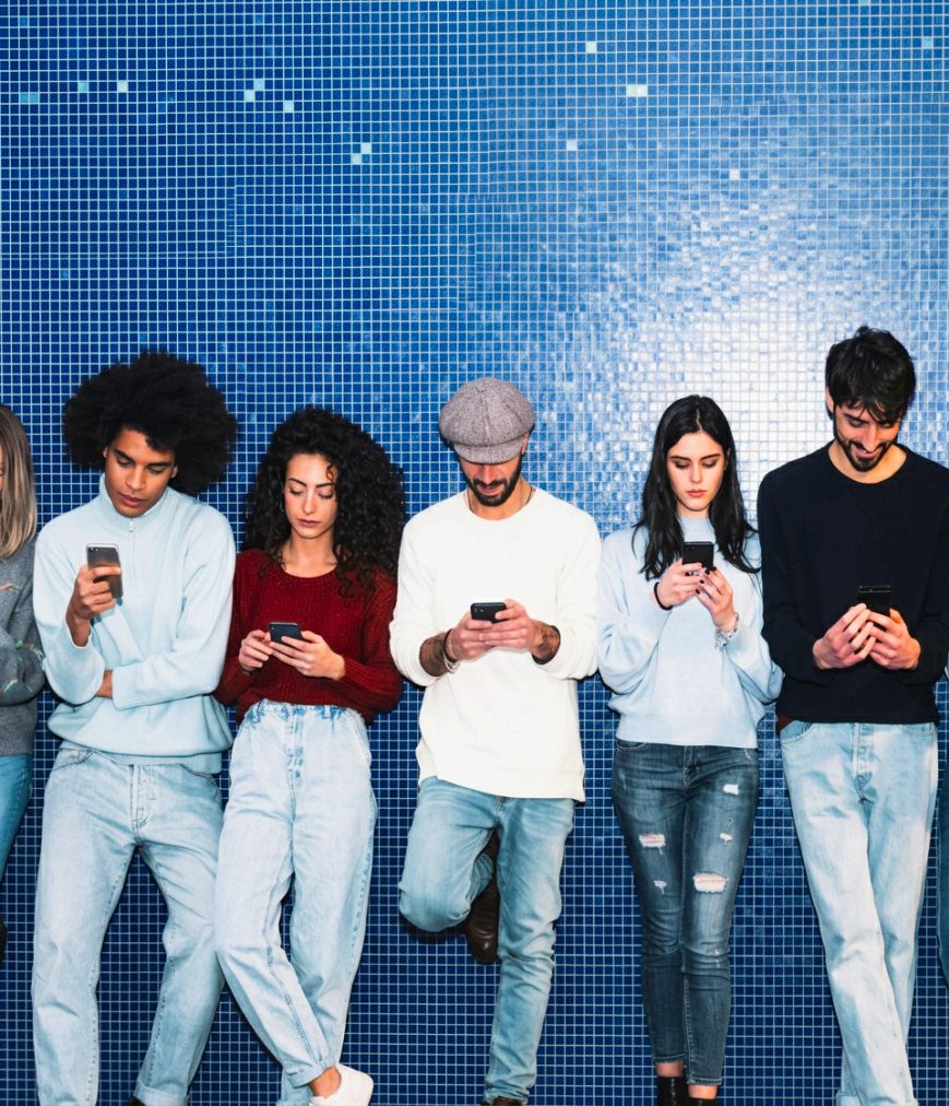 Quatro pessoas olhando para seus celulares encostadas em uma parede de azulejos